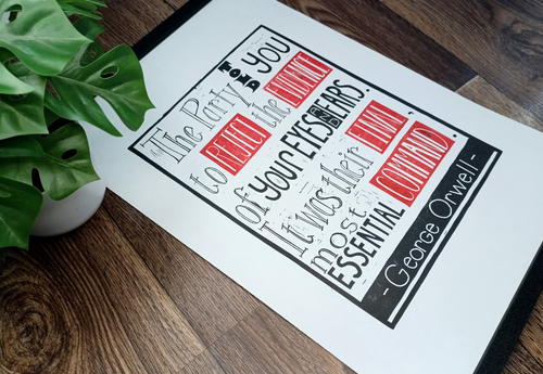 Printed quote by George Orwell on a wooden surface with a plant.